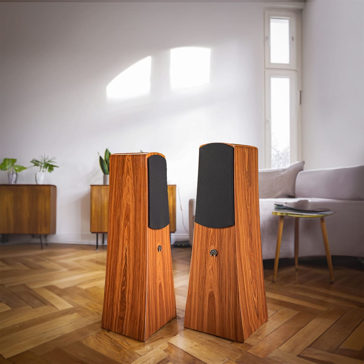 A pair of Alec loudspeakers in a rosewood finish standing on a herringbone floor in a bright living room