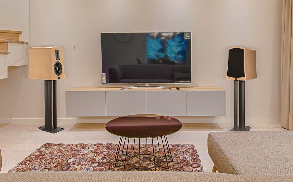 A pair of Alyssa loudspeakers on stands either side of a wall mounted screen in a bright living room